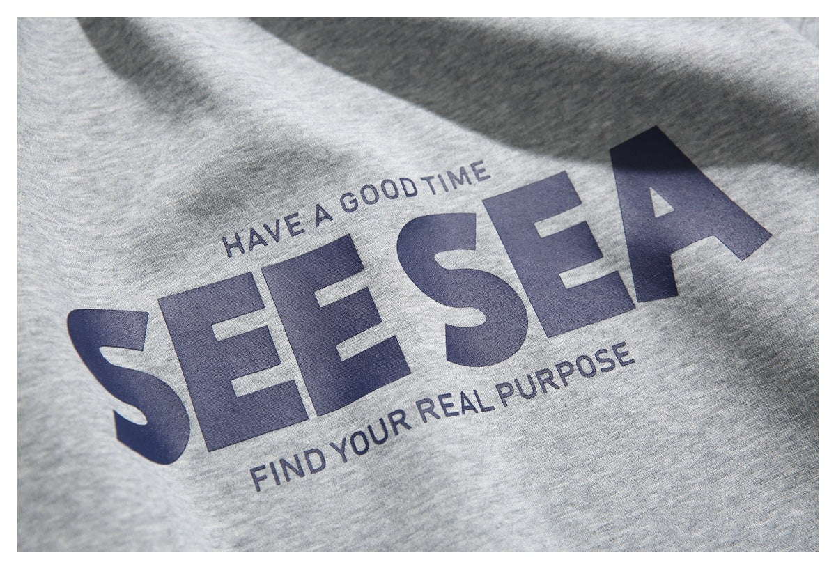 Close-up of navy “SEE SEA” lettering and smaller text printed on heather-gray sweatshirt fabric.