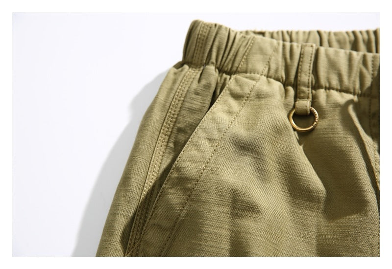 Close-up of olive shorts showing the elastic waistband, side pocket seam, and small metal ring.