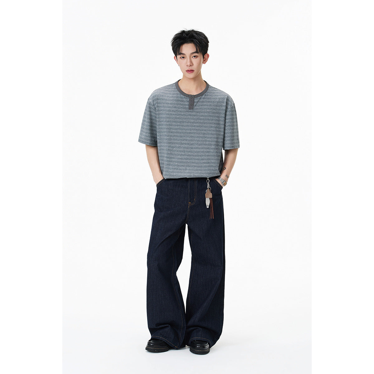 Model wearing a gray short-sleeve striped Henley with dark buttons and loose dark jeans.
