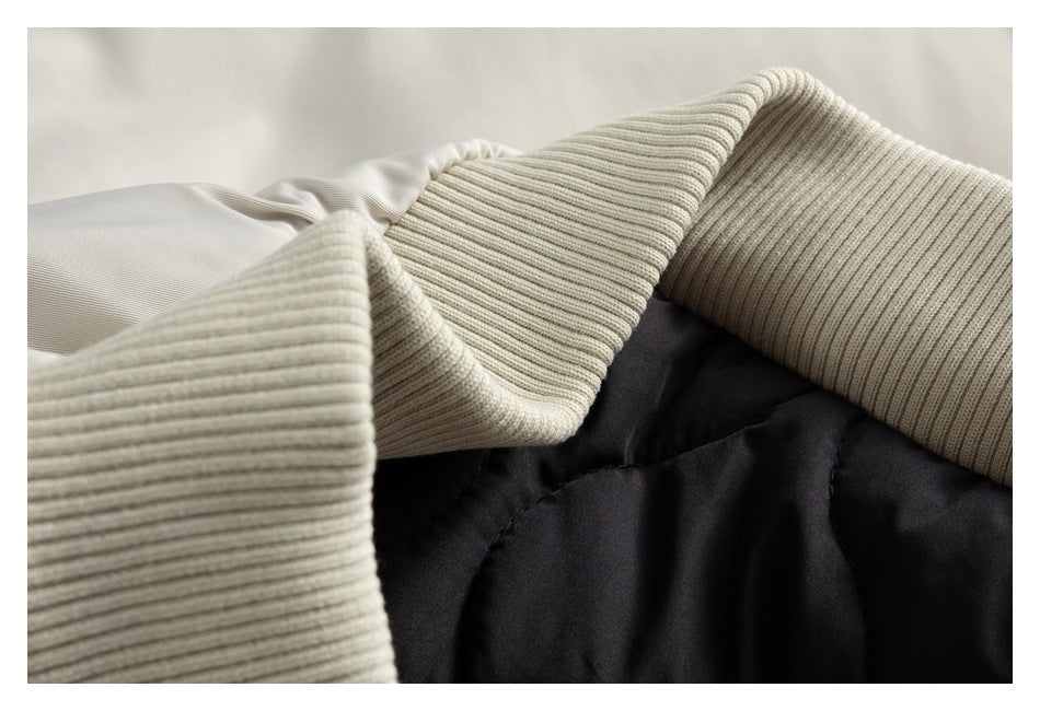 Close-up of wide ribbed ivory cuffs beside black quilted coat fabric.