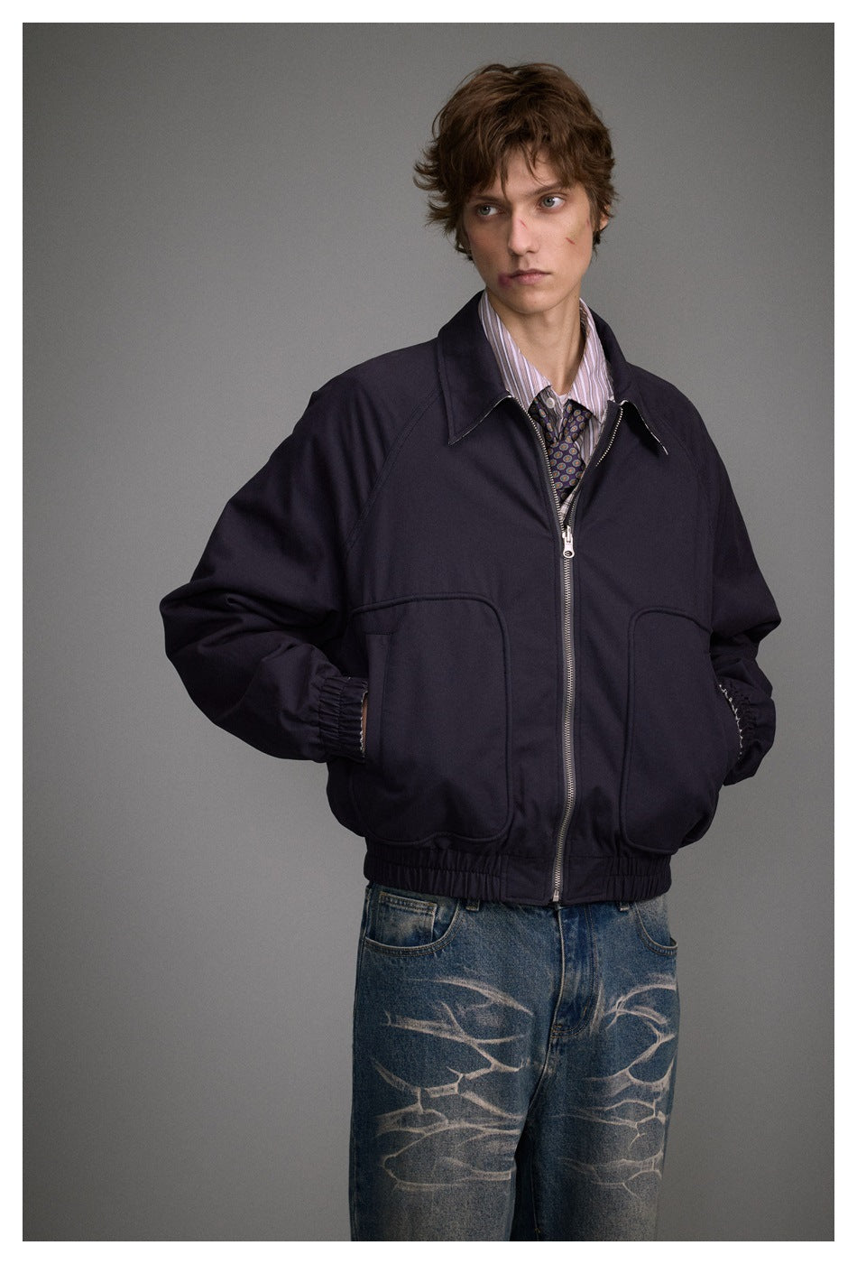 Closer view of a model wearing a dark navy zip jacket with a pointed collar, two large pockets and an elastic hem.