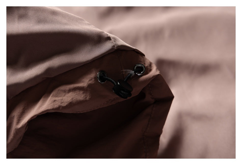 Close-up of a brown garment edge with black drawcords, eyelets, and toggles.