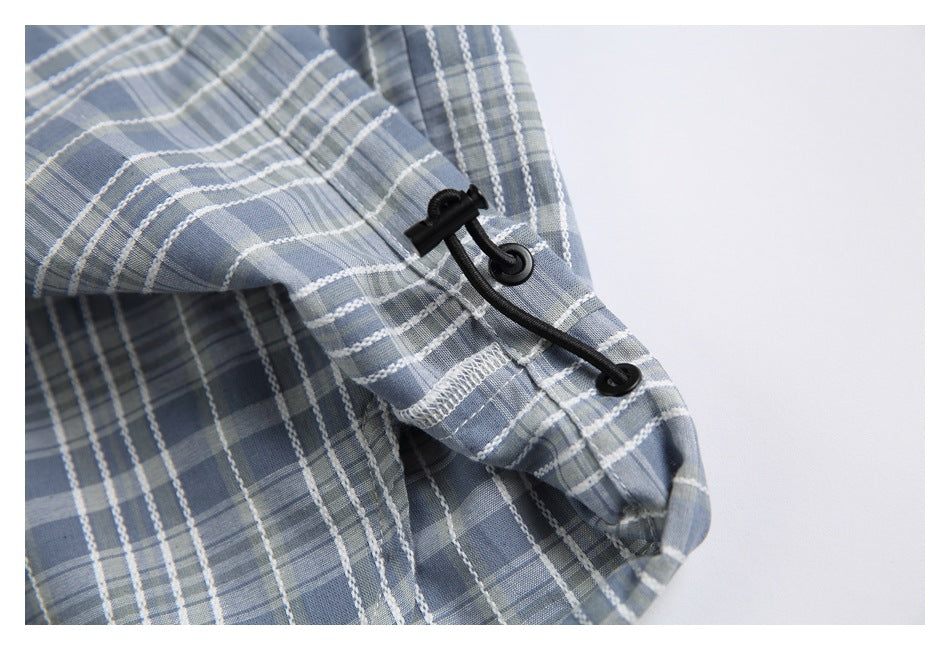 Close-up of a black elastic drawcord and eyelets on the blue-gray plaid garment.