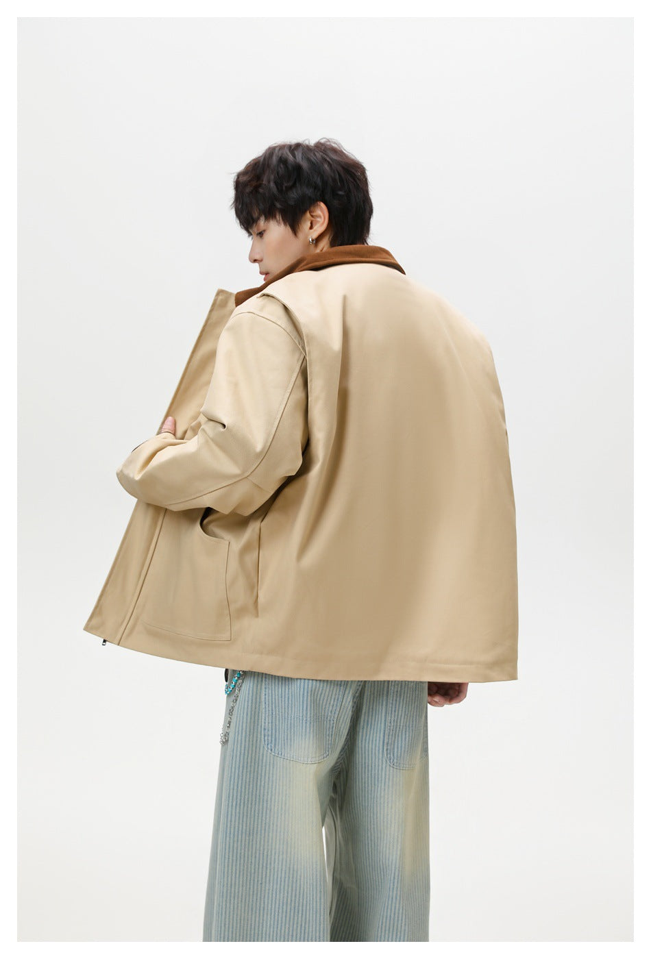 Rear three-quarter view of a model wearing a beige jacket with a brown collar and a large plain back panel.