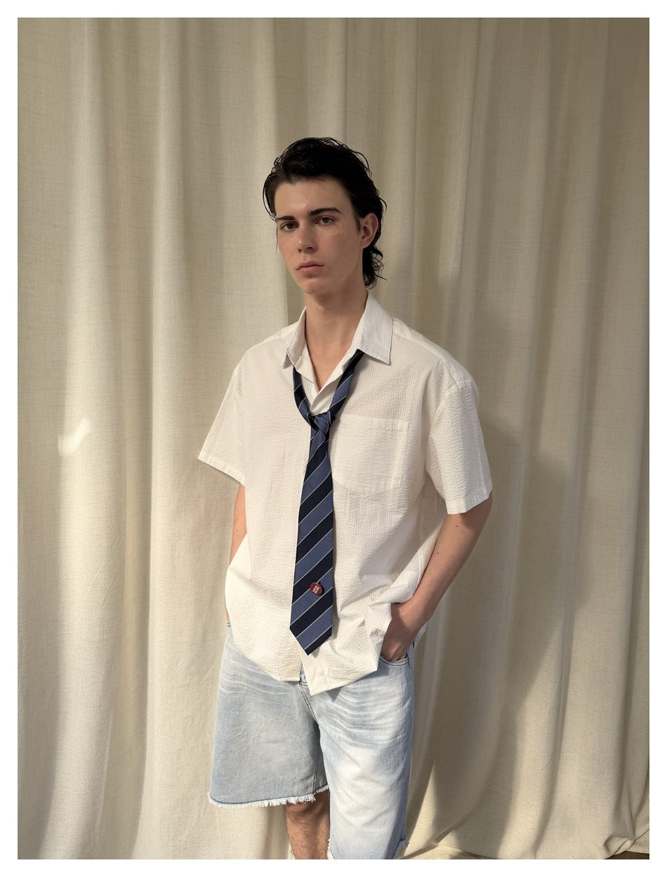 Model wearing a white short-sleeve collared shirt with a chest pocket and striped navy tie.