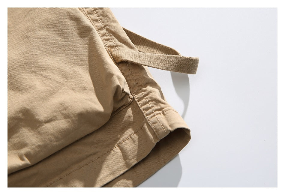 Close-up of the tan shorts' hem, side seam and attached fabric strap.