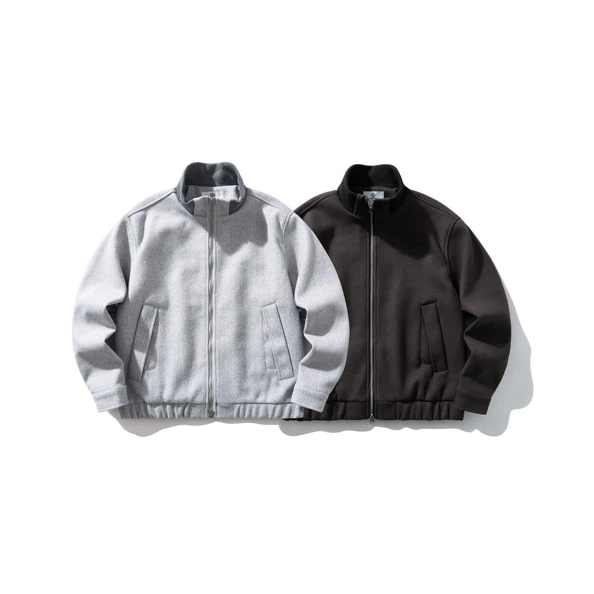 Two zip-front jackets shown from the front in light gray and dark charcoal, with stand collars and slanted pockets.
