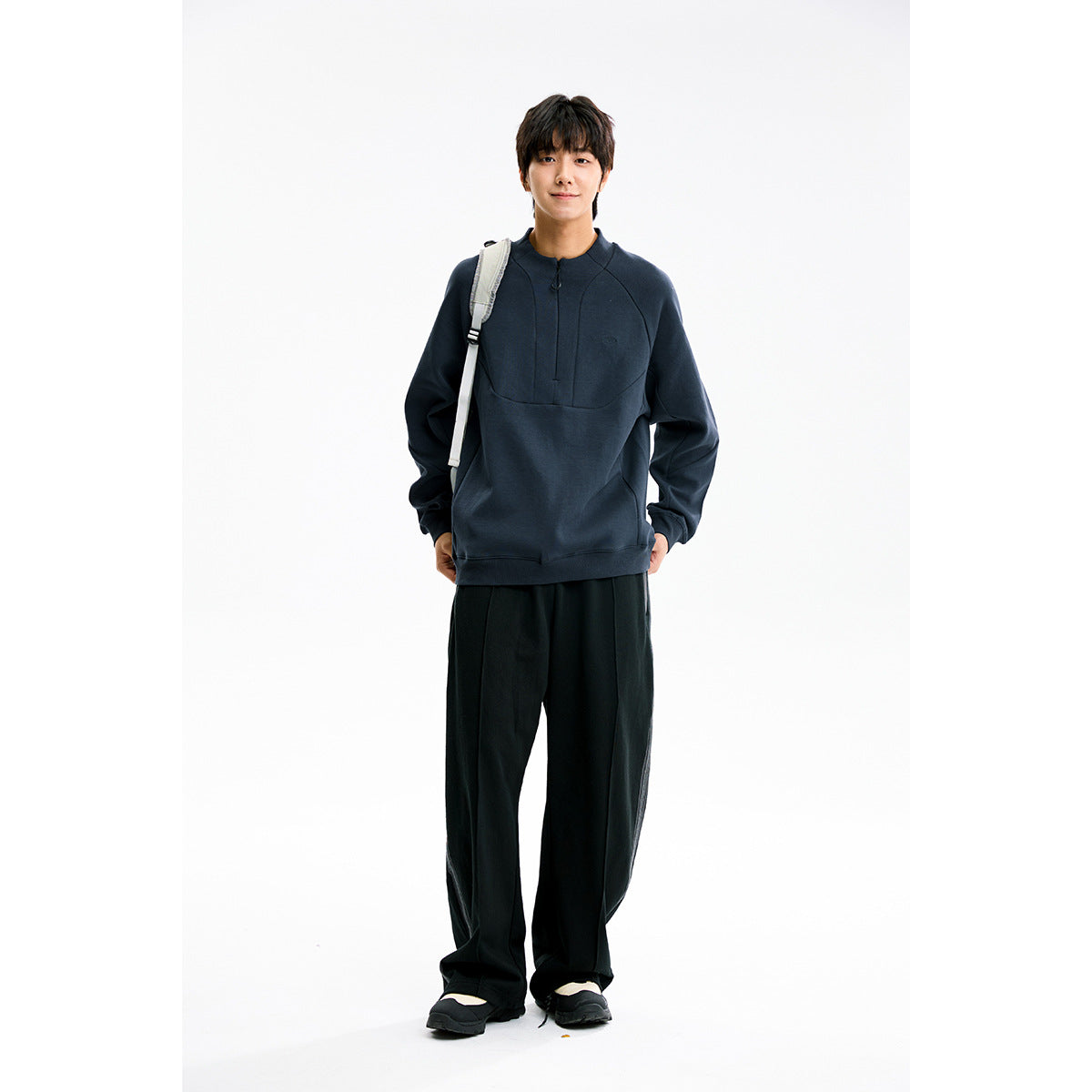 Full-length view of a model wearing a dark navy high-neck pullover with a short front zipper and black wide-leg pants.