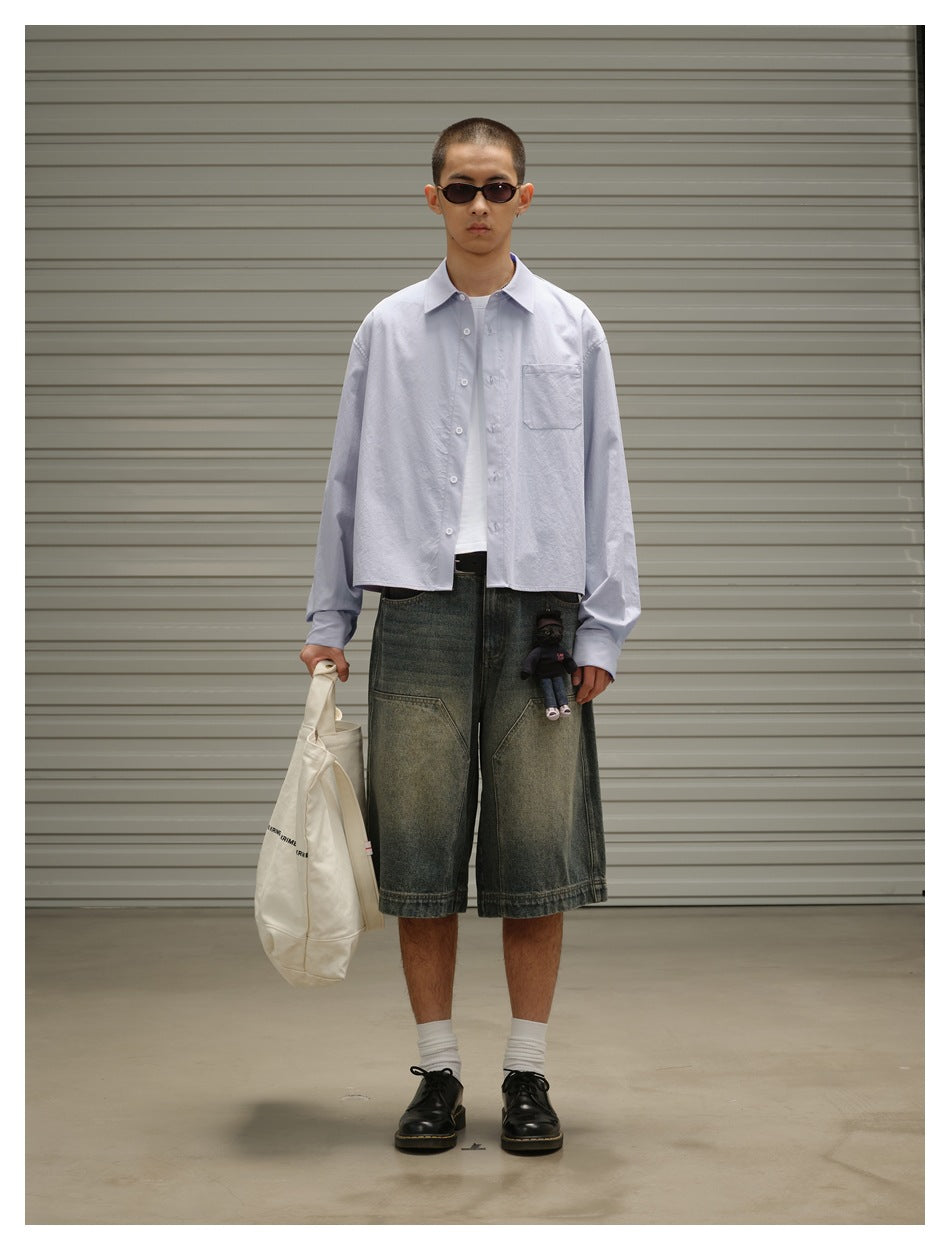 Full-length view of a model wearing a pale blue button-up shirt with a chest pocket and oversized dark denim shorts.