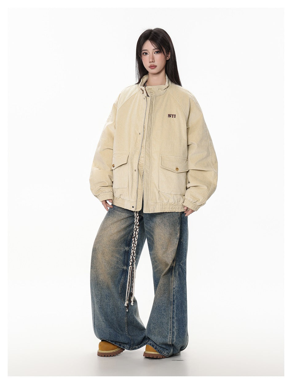 Full-length front view of a model wearing a beige oversized jacket with flap pockets and wide-leg faded blue jeans.