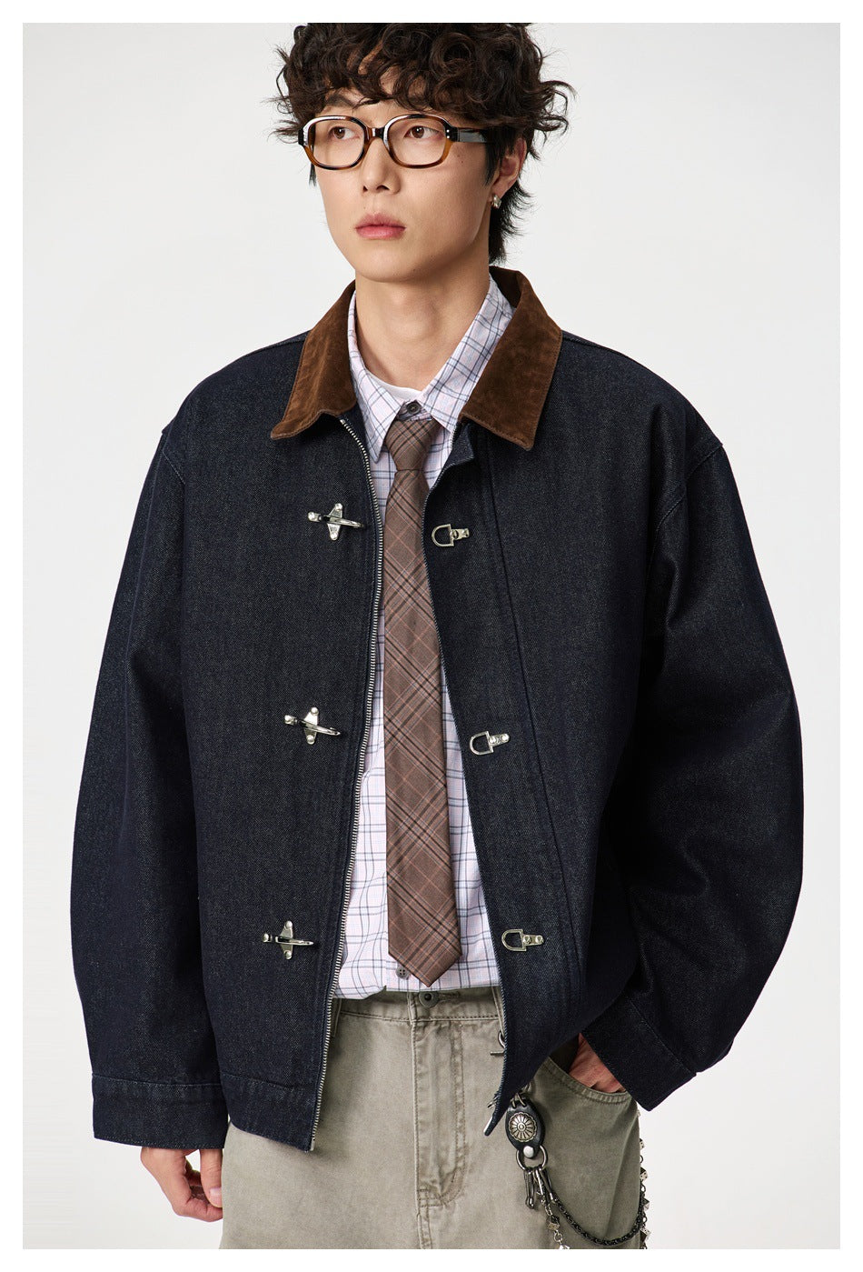 Close view of a model wearing a dark indigo jacket with a brown collar and silver toggle closures over a plaid shirt.