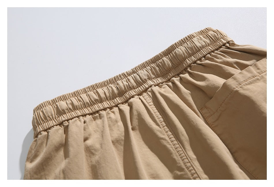 Close-up of tan shorts with a gathered elastic waistband and part of a pocket.