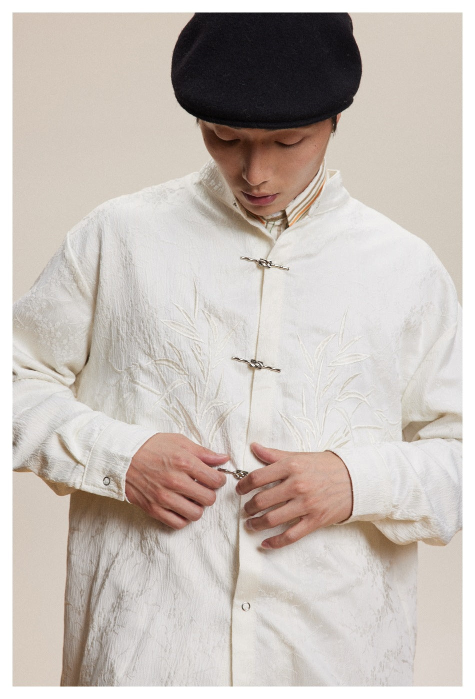 Close view of ivory jacket’s tonal bamboo embroidery, stand collar, cuffs and metal frog closures.