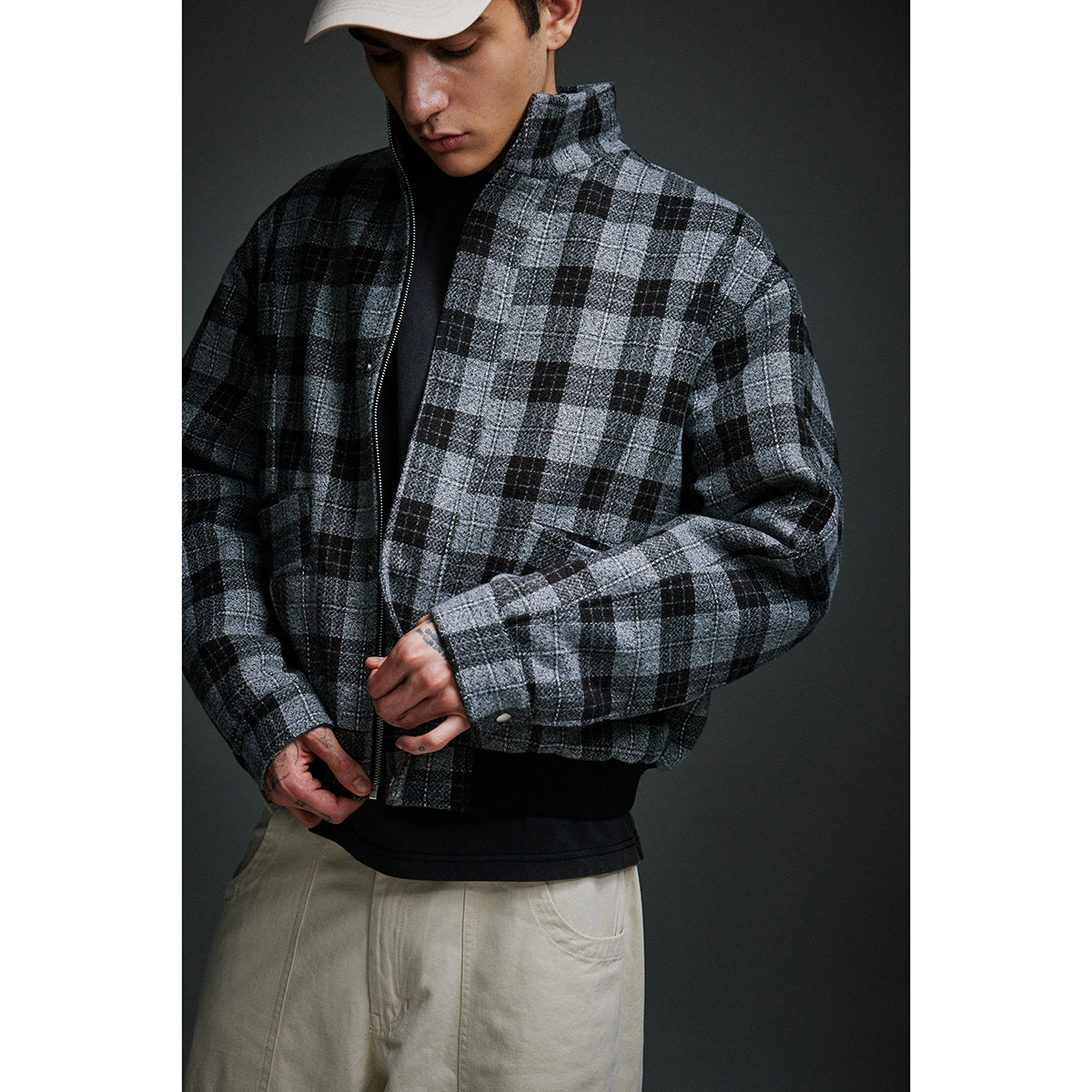 Close-up of a model wearing a gray-and-black plaid zip jacket, showing its raised collar, zipper, cuffs, and ribbed hem.