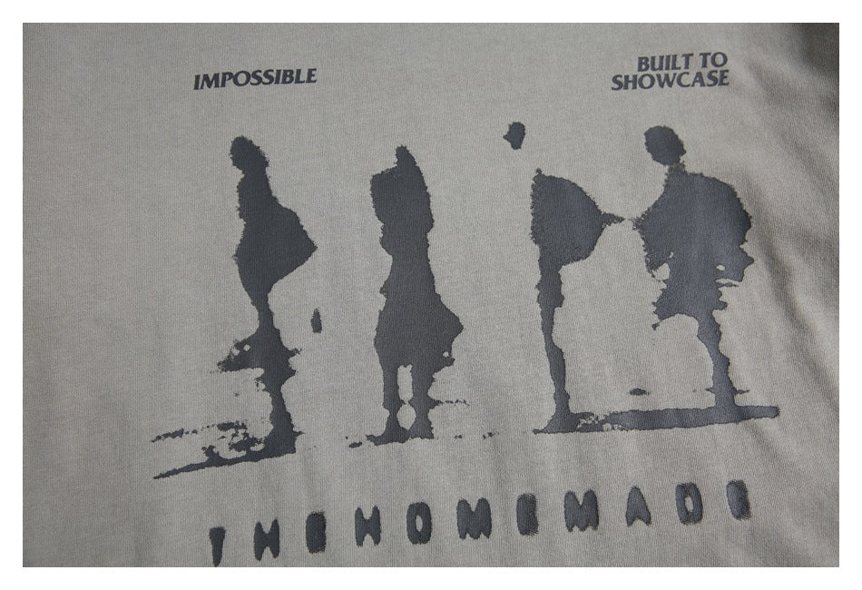 Close-up of a gray T-shirt graphic with dark silhouettes and English text reading “IMPOSSIBLE” and “BUILT TO SHOWCASE.”