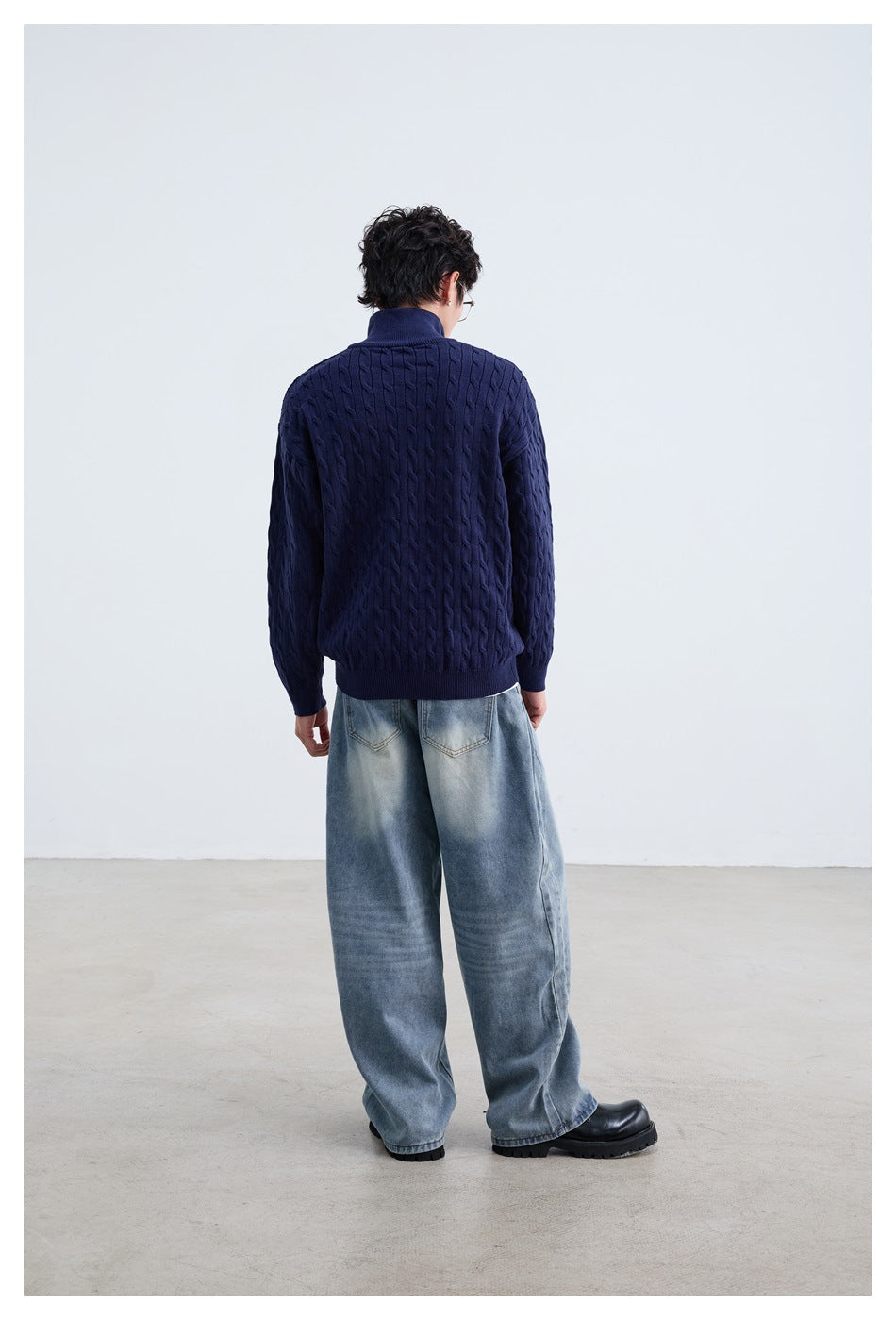 Rear view of a model wearing a navy cable-knit sweater with ribbed hem and cuffs, paired with light-wash jeans.