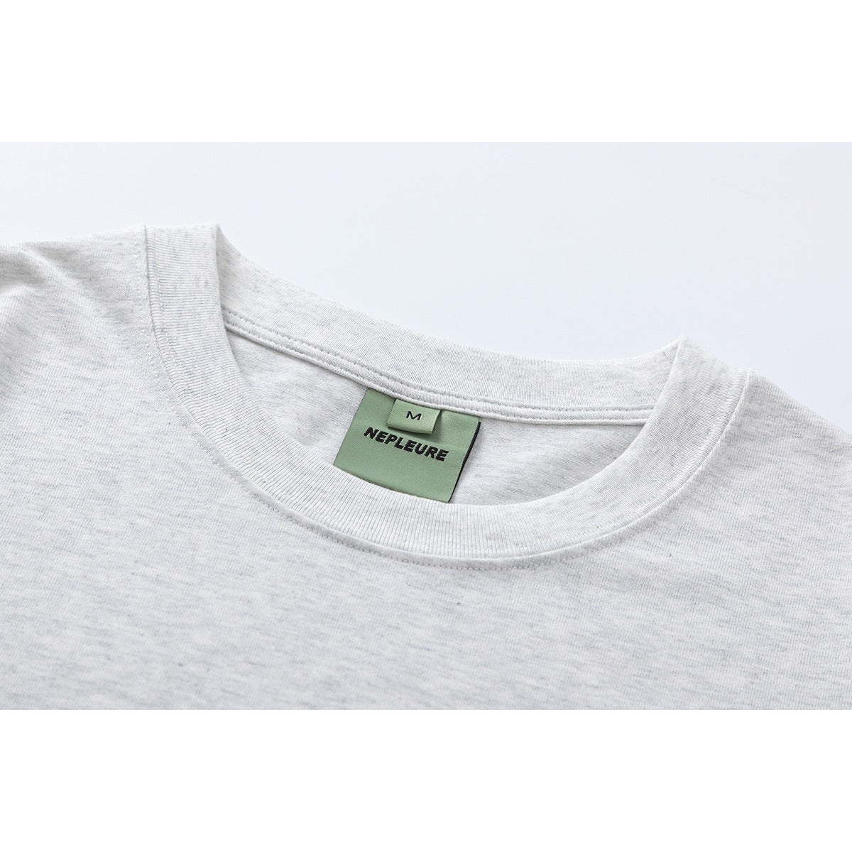 Close-up of a light heather gray T-shirt crew neck and green NEPLEURE size M label.