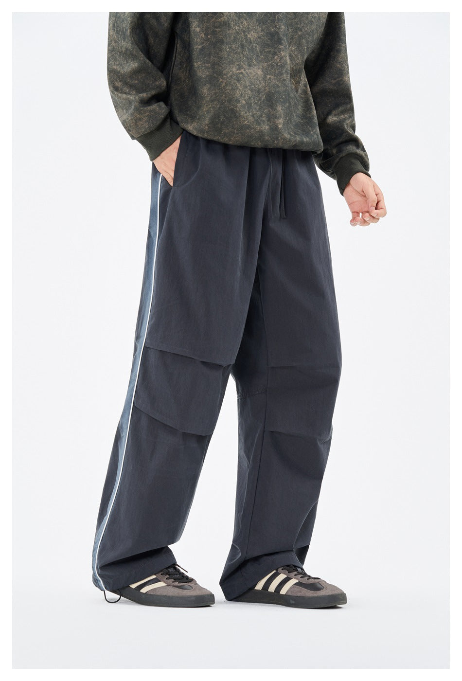 Front view of a model wearing loose navy pants with a drawstring waist, layered leg panels, and light side piping.