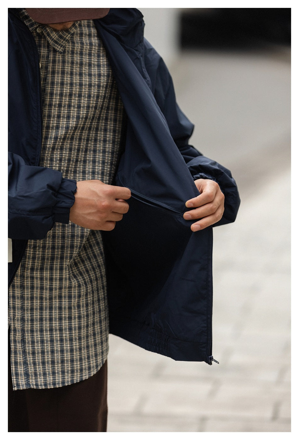 Close-up of a person opening the navy jacket to show a horizontal zippered inner pocket.