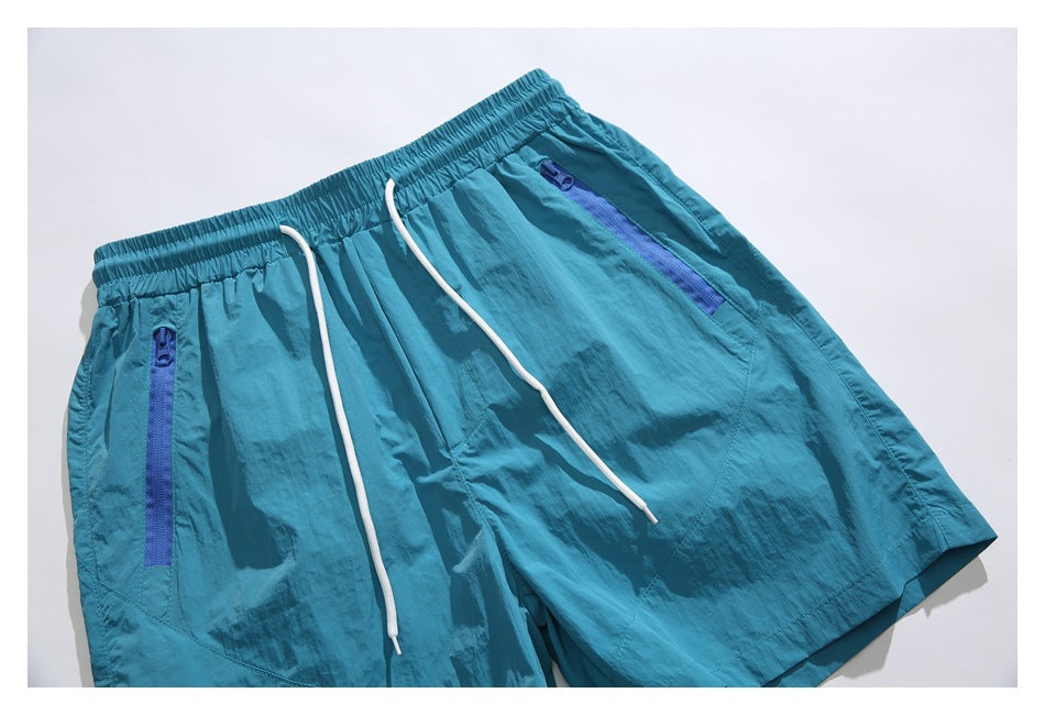 Close-up of turquoise shorts showing the elastic drawstring waist and two blue zip pockets.