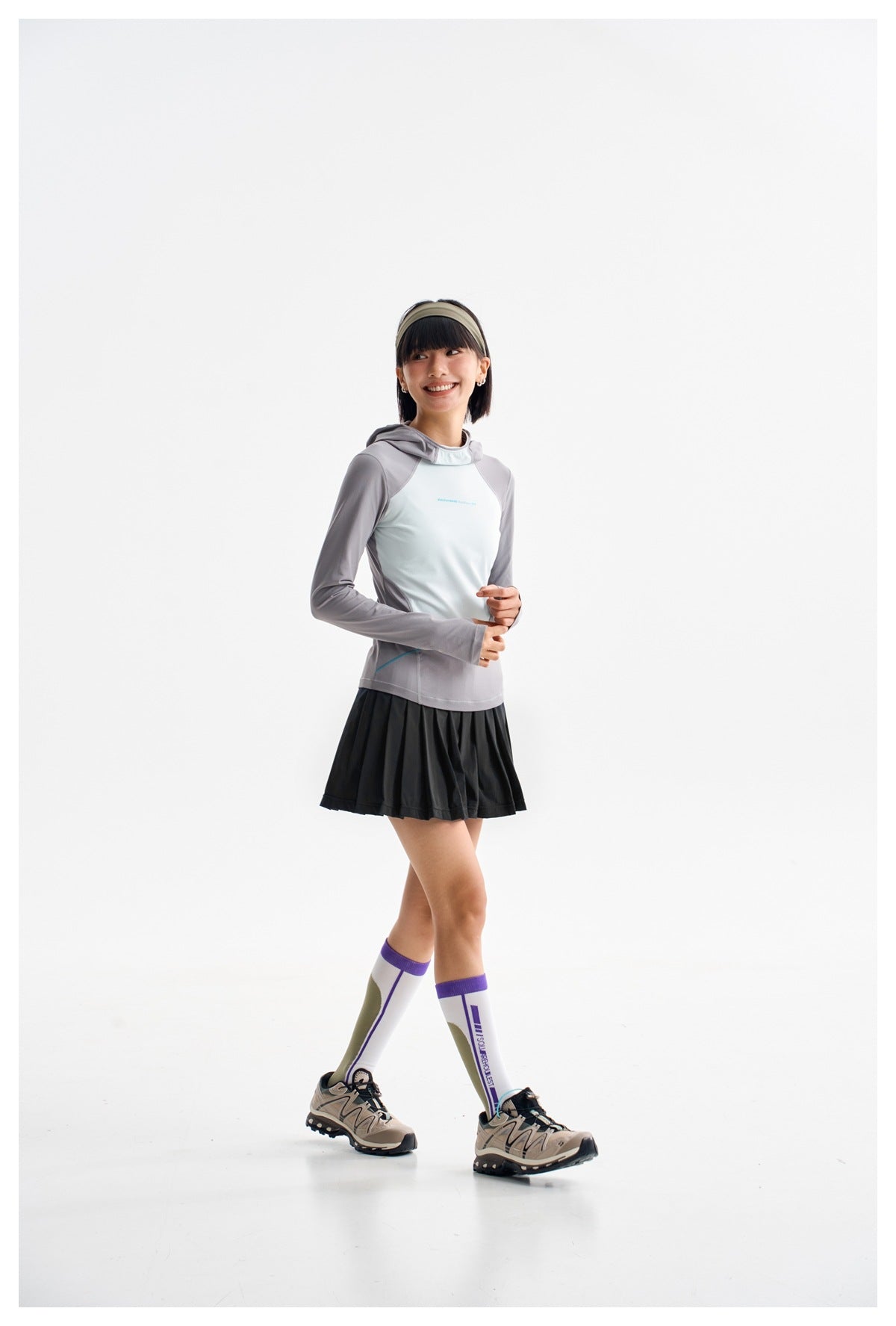 Model wearing a black pleated athletic skirt and a gray-and-pale-blue hooded top.