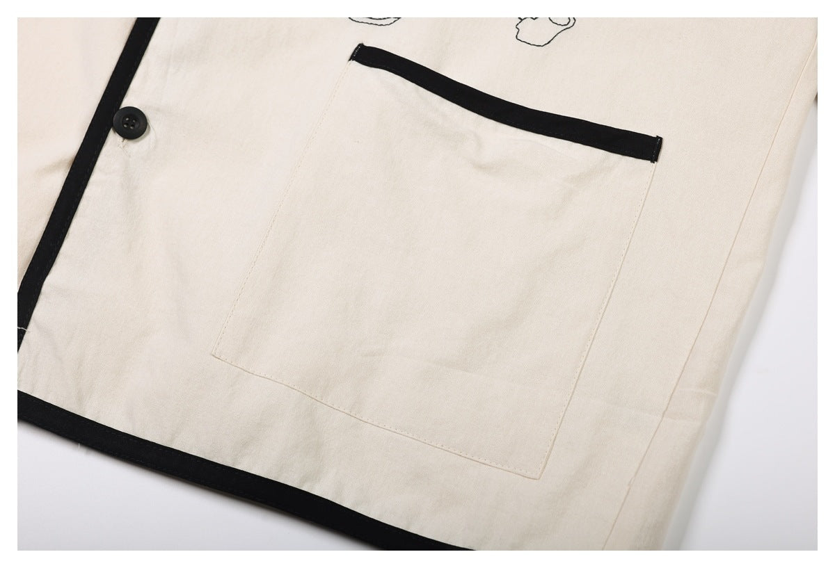 Close-up of a cream garment with black piping, a black button, and a large pocket.