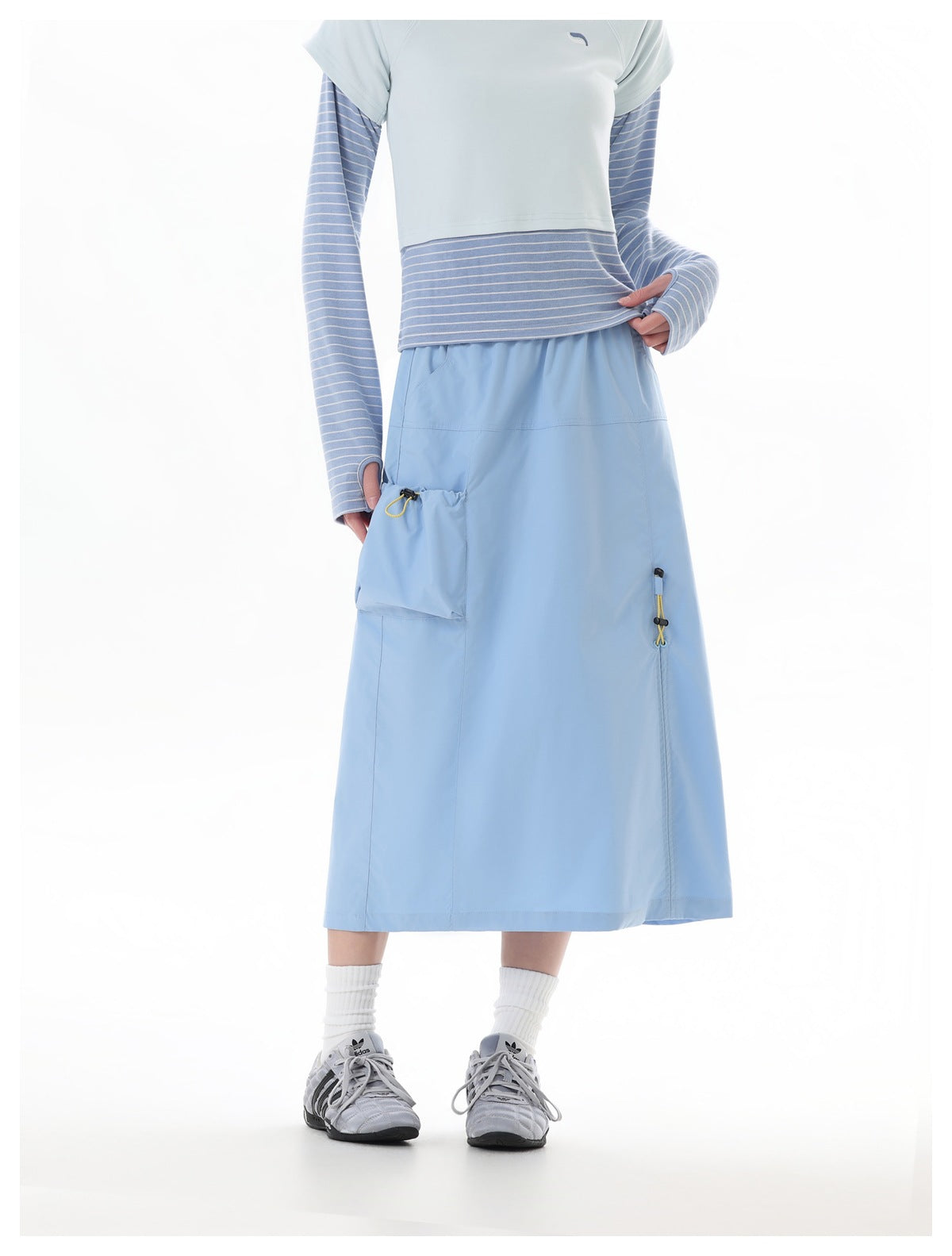 Front view of a model wearing a light blue midi skirt with a large utility pocket and yellow drawcord details.