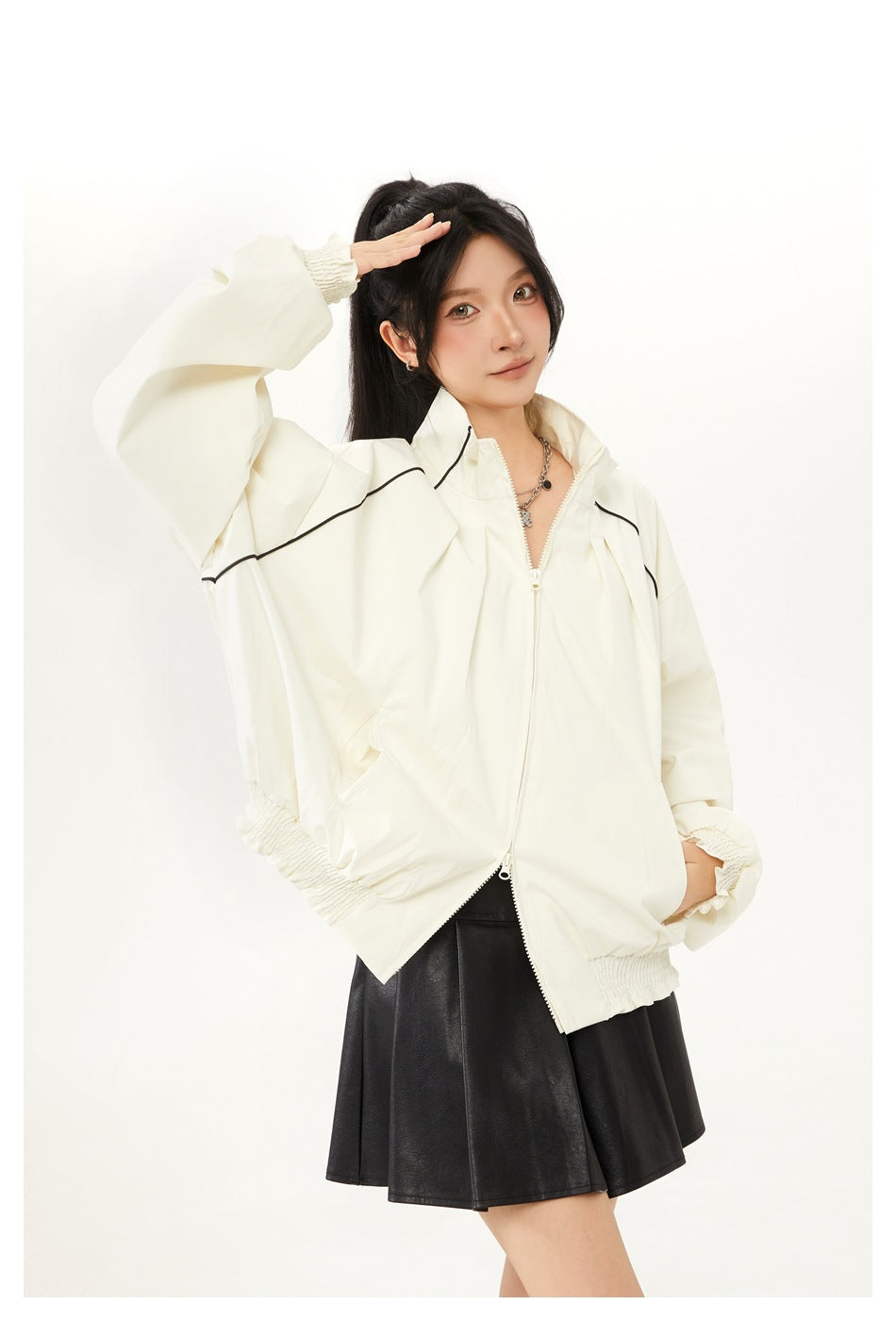 Closer view of a model wearing an ivory zip jacket with black piping and smocked cuffs, paired with a black skirt.