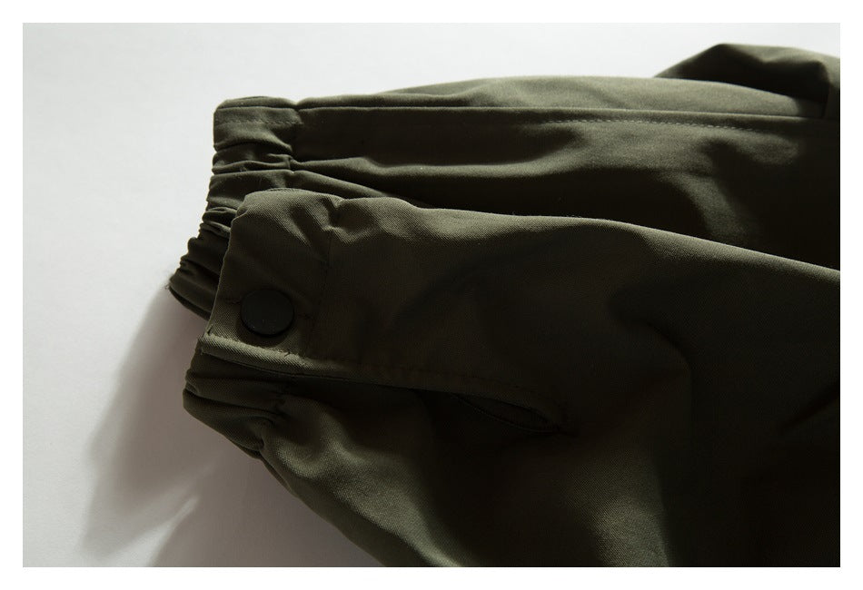 Close-up of an olive jacket sleeve cuff with a black snap and gathered fabric.