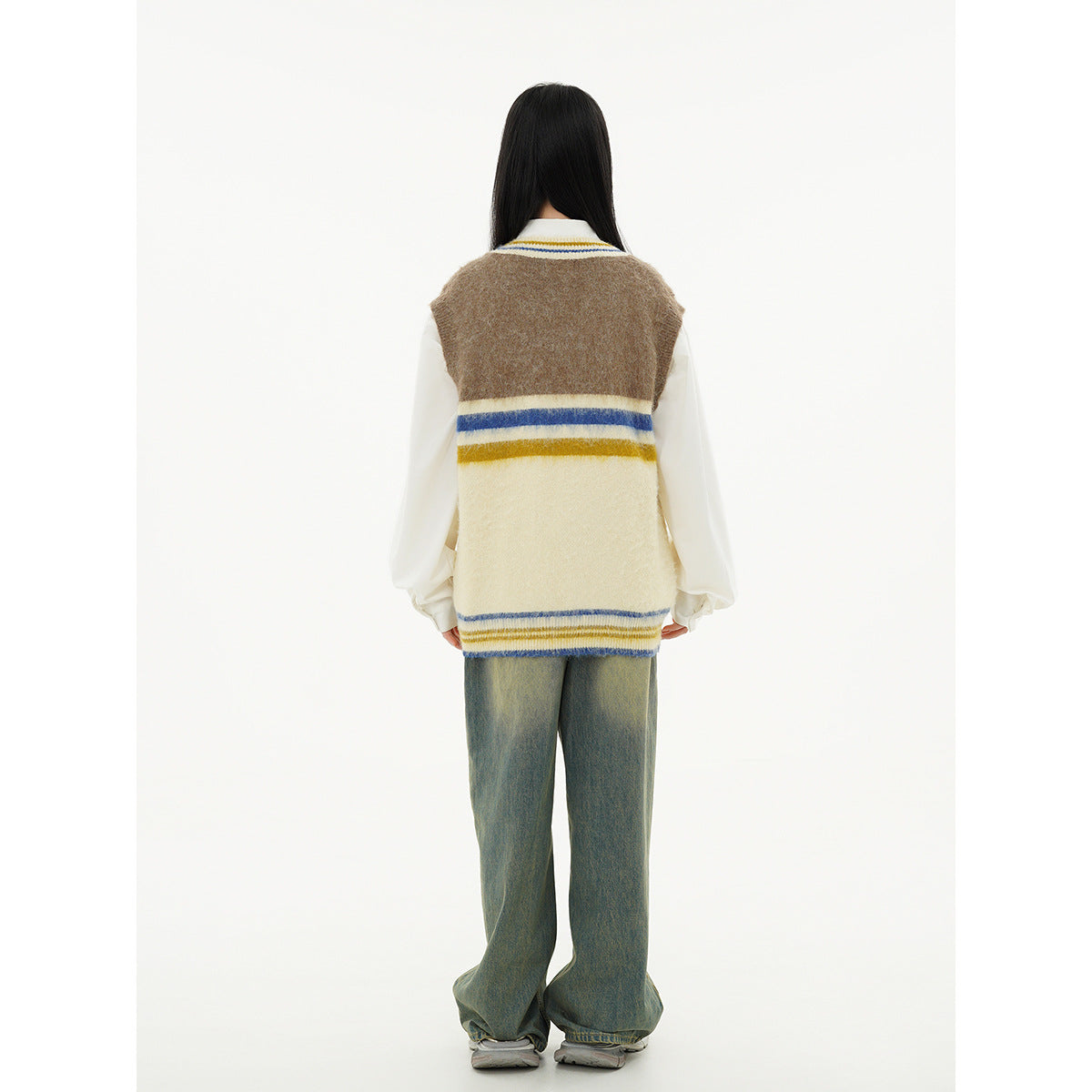 Back view of a model wearing a brown and cream sweater vest with blue and yellow stripes over a white shirt.