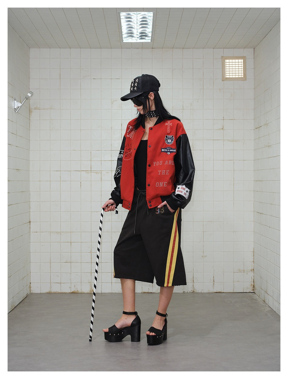 Model wearing a red-and-black varsity jacket with patches and lettering, black shorts with striped sides, and platform