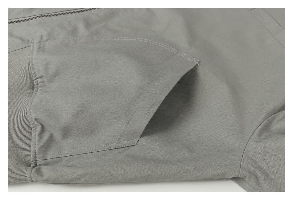 Close-up of a gray jacket pocket opening, stitching, and ribbed hem beside the zipper.