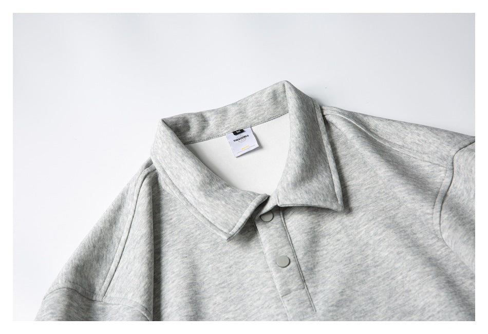Cropped front view of a light heather-gray polo shirt showing its collar and snap-button placket.