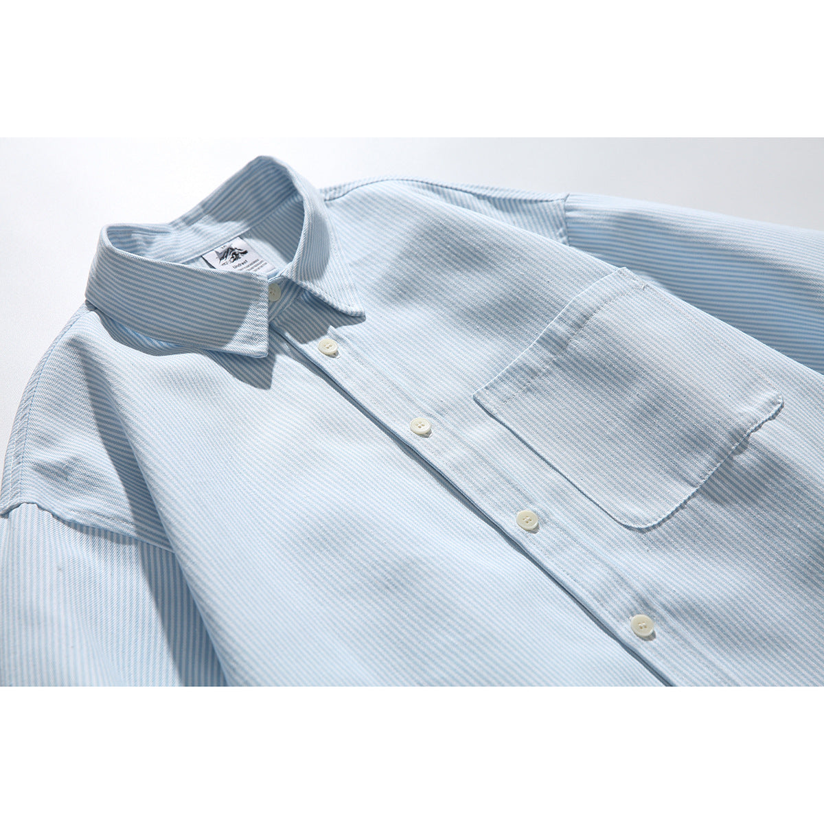 Close-up of a pale blue and white striped button-up shirt showing its collar, buttons, and chest pocket.