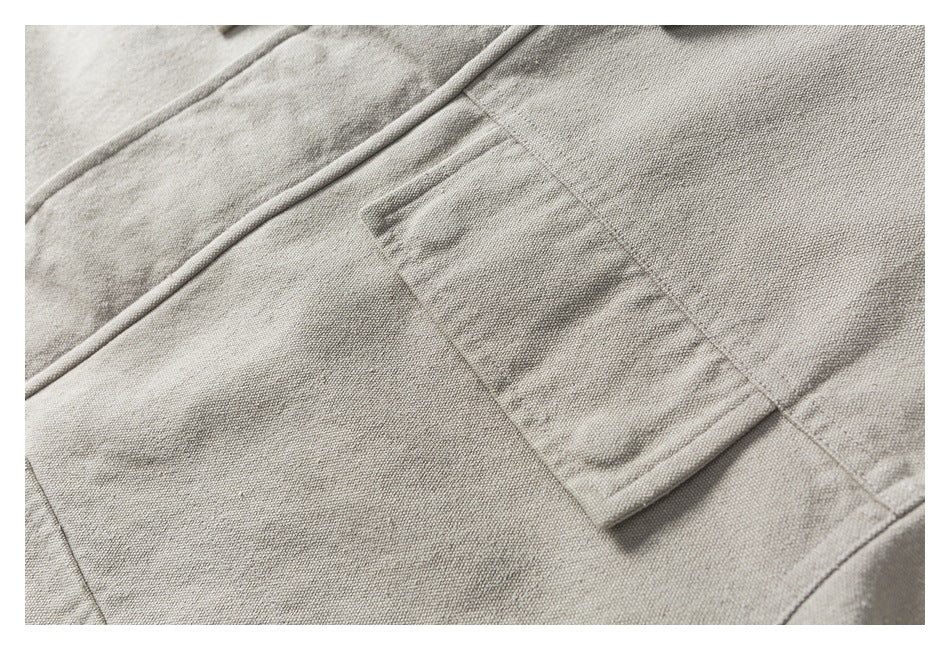 Close-up of a small beige flap pocket and seams on textured jacket fabric.