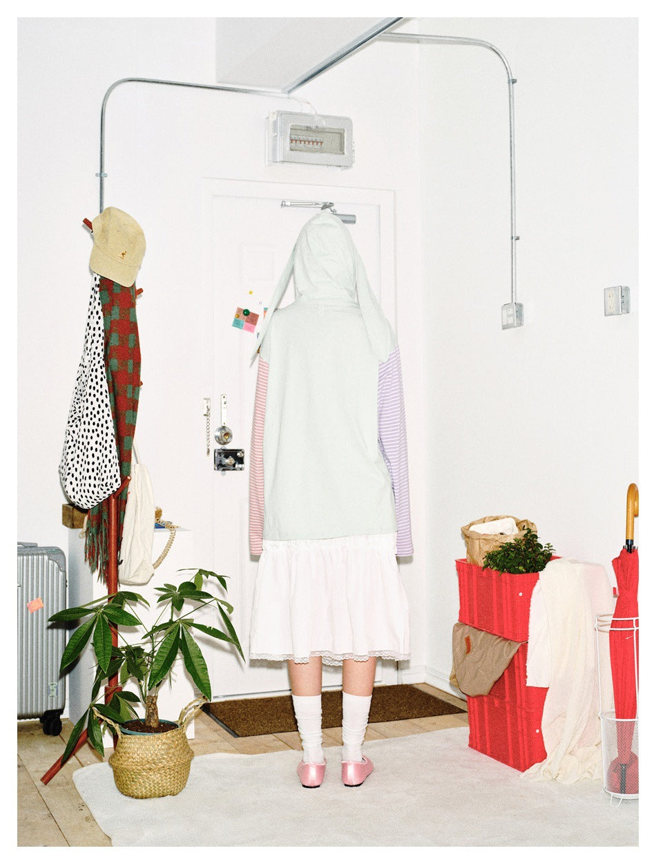 Back view of a person wearing a pale mint bunny-ear hooded top with pink and lavender striped sleeves and a white skirt.