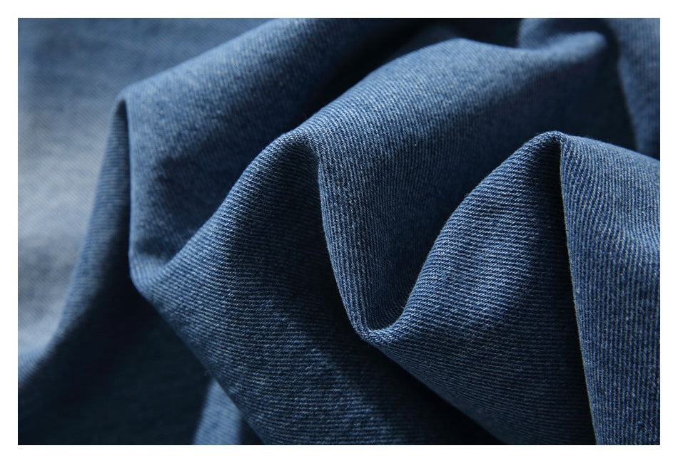 Close-up of blue denim fabric folded into soft ridges, showing its diagonal weave.