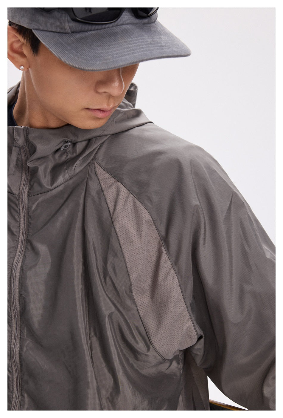 Close-up of a dark gray hooded jacket showing its zipper, drawcord, and mesh underarm panel.