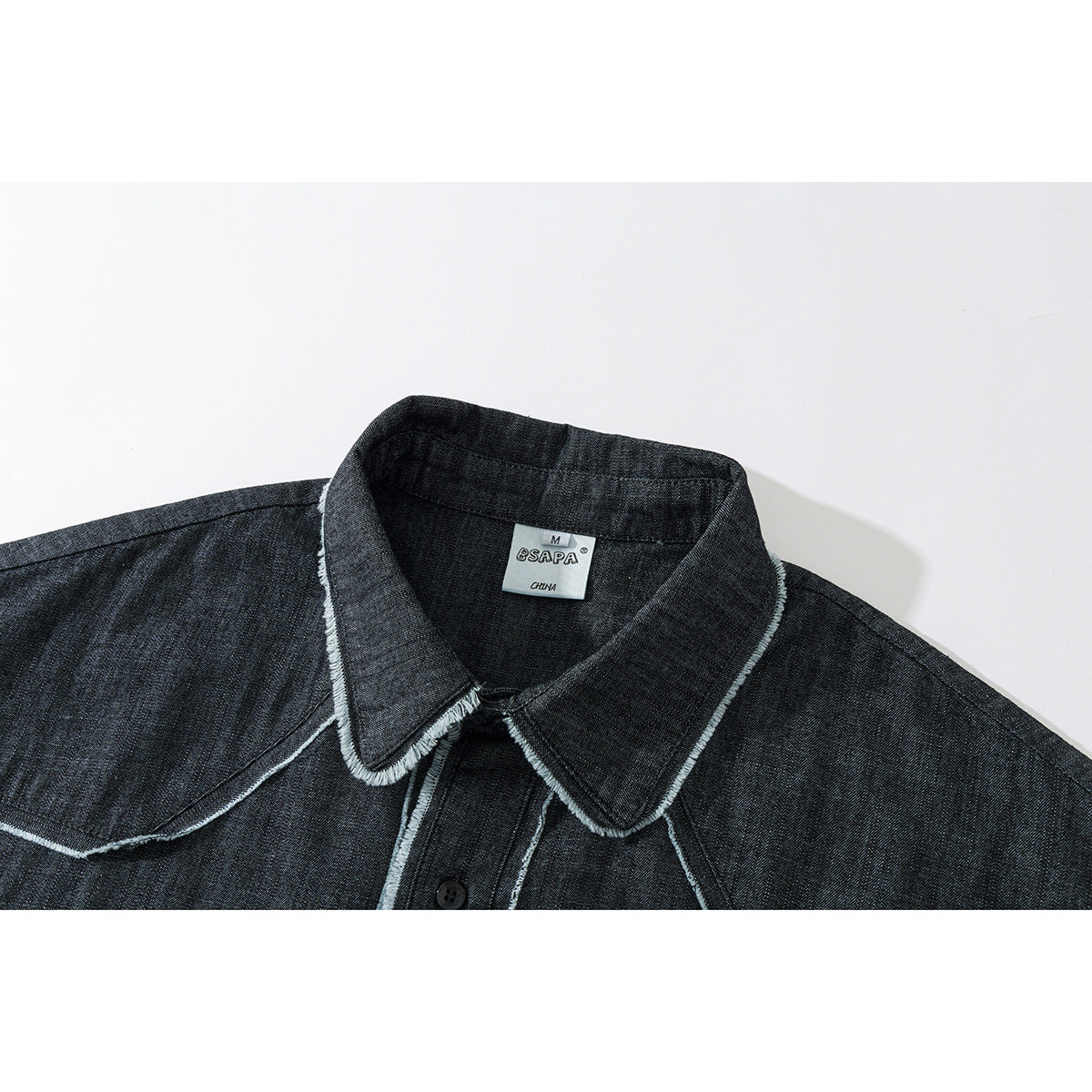 Close-up of a charcoal denim shirt collar with pale frayed-edge stitching and a visible neck label.