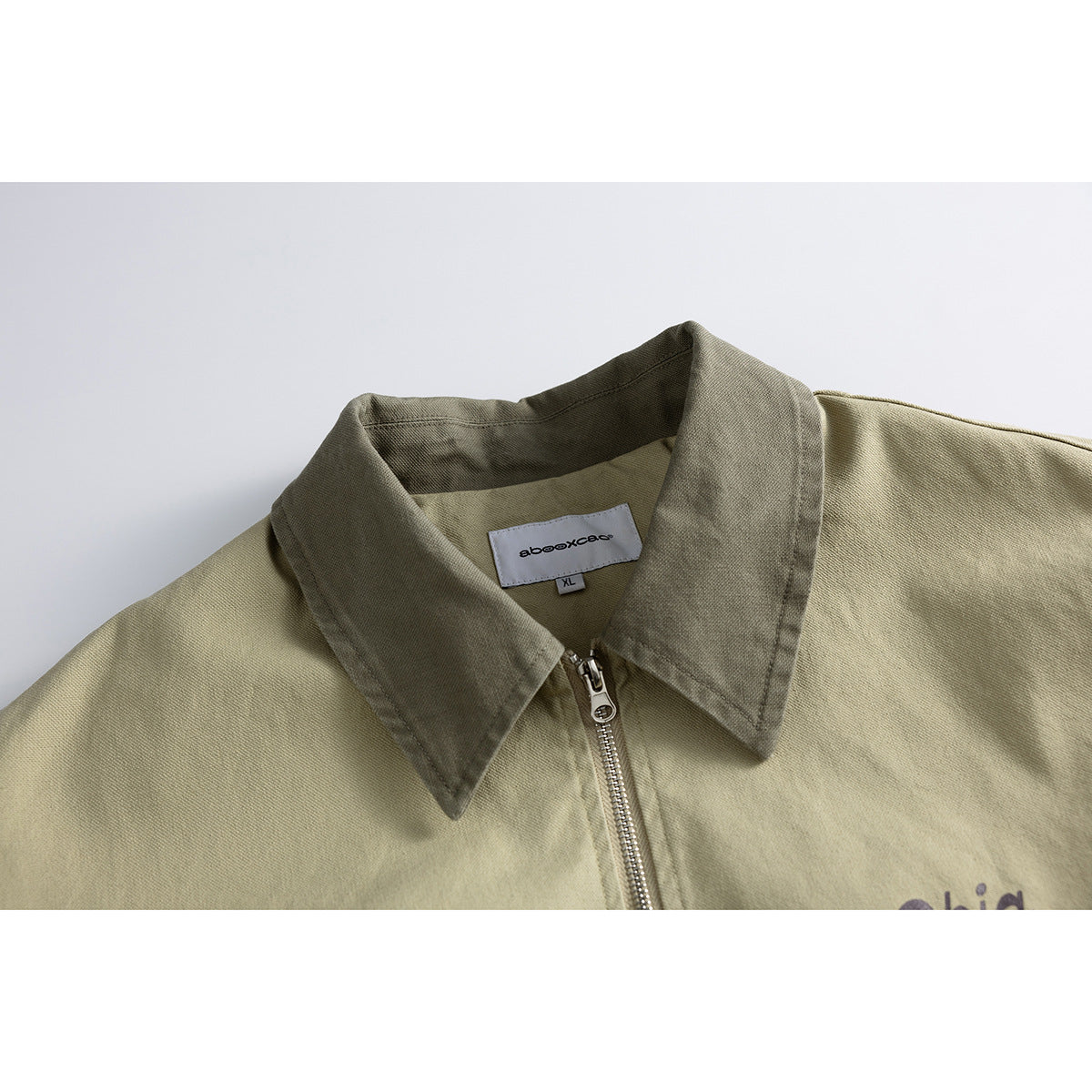 Close-up of a khaki zip-front jacket with a dark olive pointed collar and visible neck label.