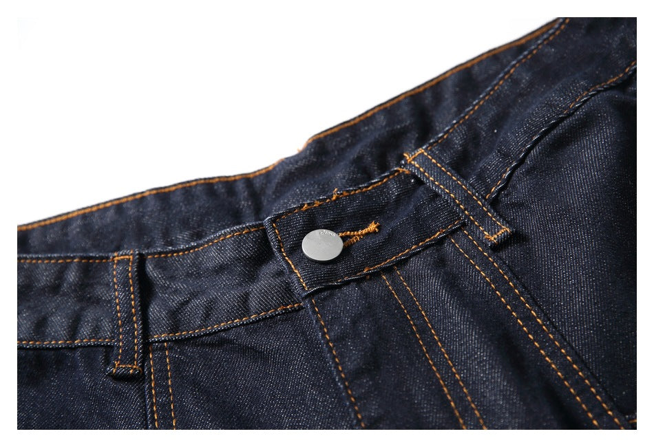 Close-up of the dark denim waistband, button closure, belt loop and orange contrast stitching.