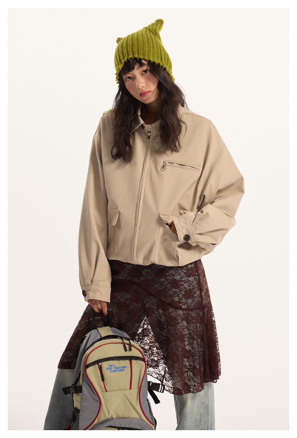 Model wears a light beige zip jacket with a chest zipper and flap pockets, paired with a dark lace skirt and lime-green