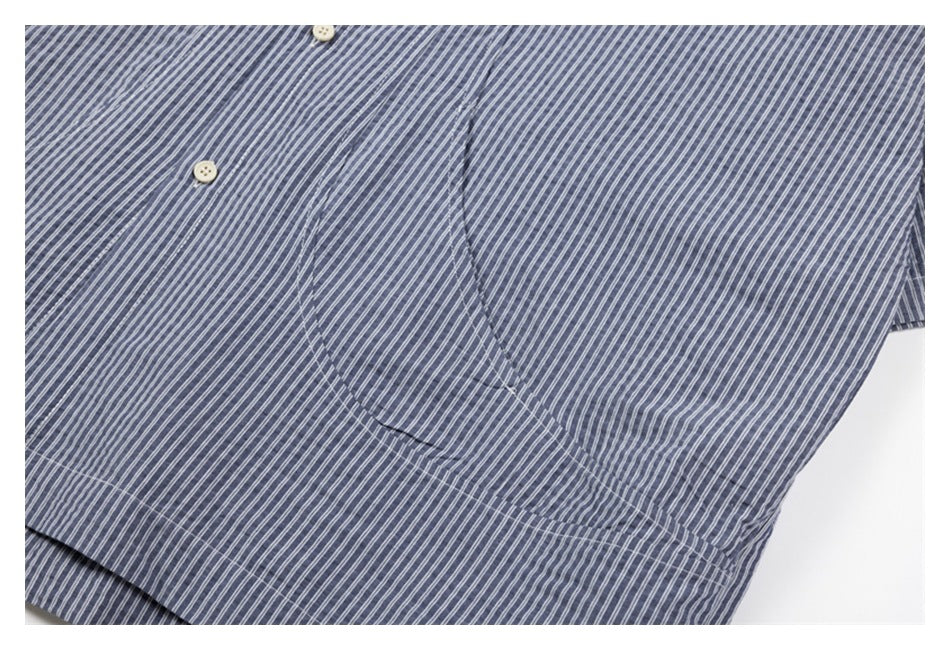 Close-up of a stitched patch pocket on the blue-gray shirt with narrow white stripes.