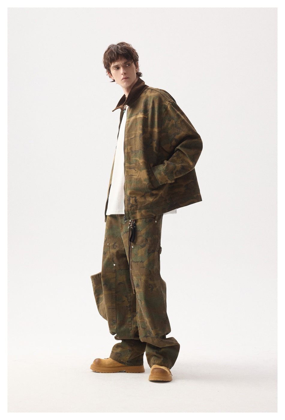 Full-length view of a model wearing a brown-green camouflage jacket and loose matching trousers with tan boots.