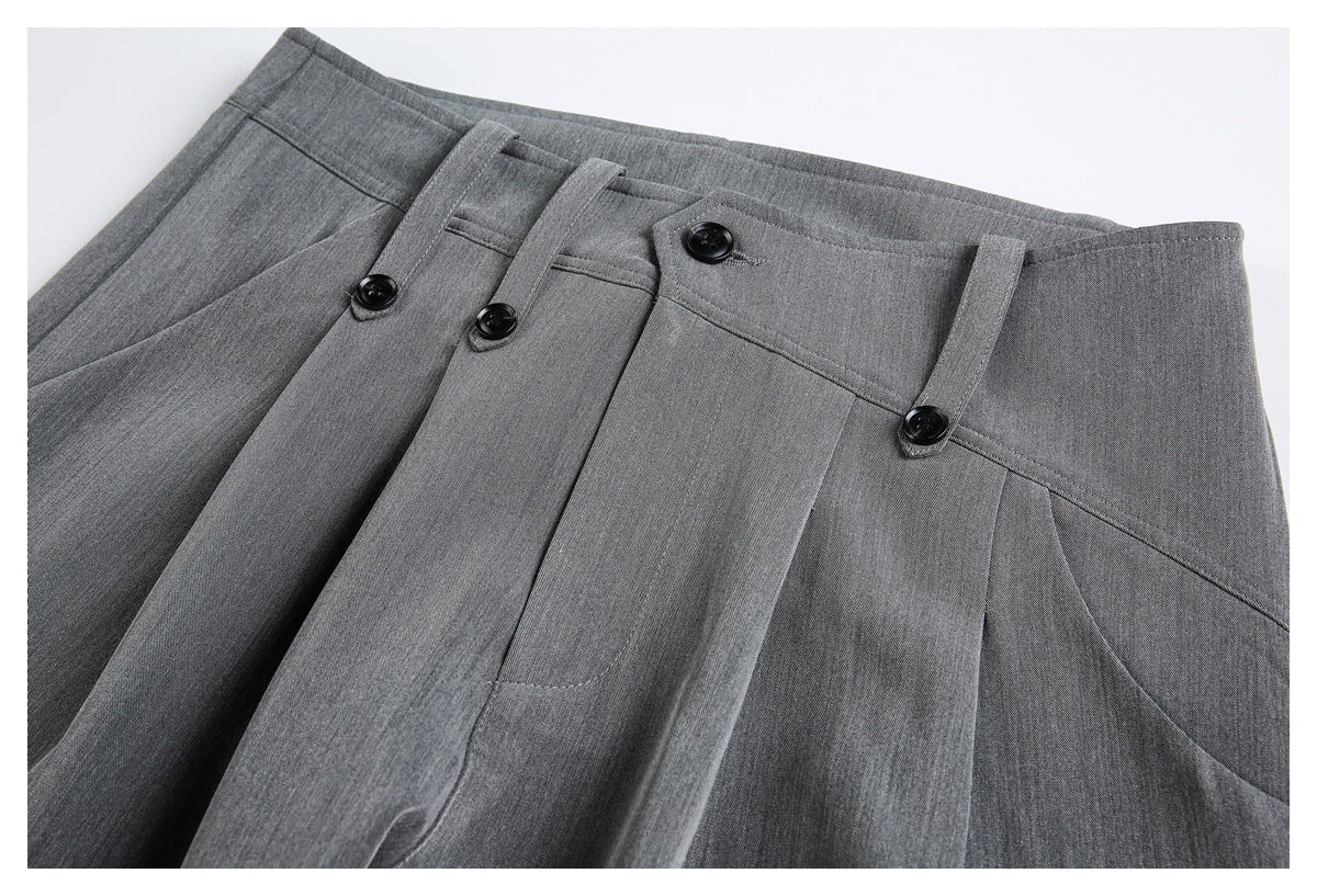 Close-up of gray trouser waist, pleats, belt loops, and black buttons.