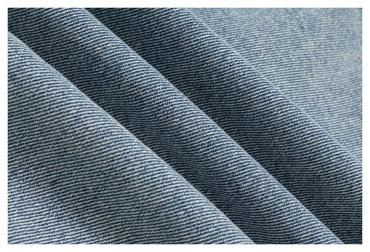 Macro view of blue denim fabric folded into ridges, showing its diagonal weave.