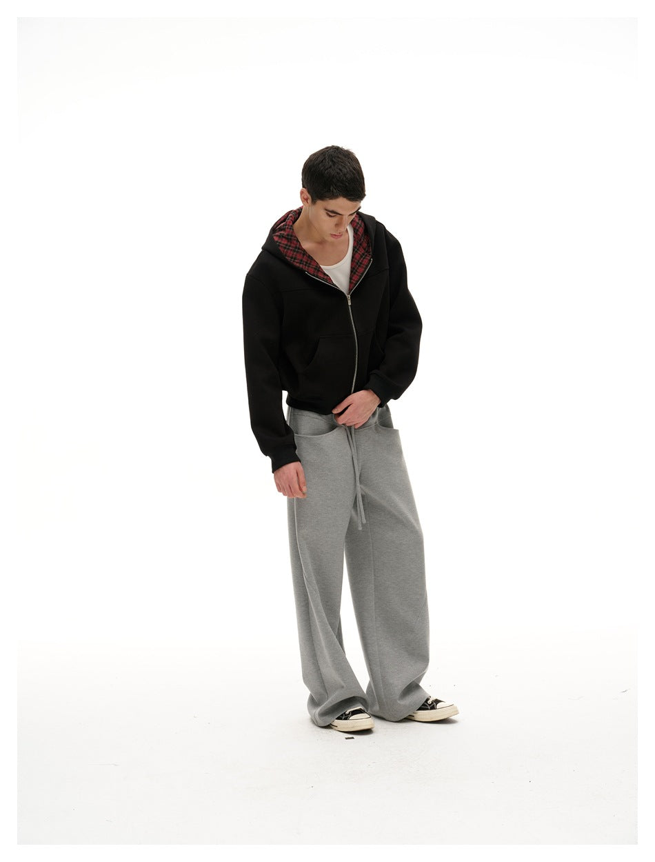 Model looking down in a black zip-up hoodie with red plaid lining and loose gray drawstring pants.