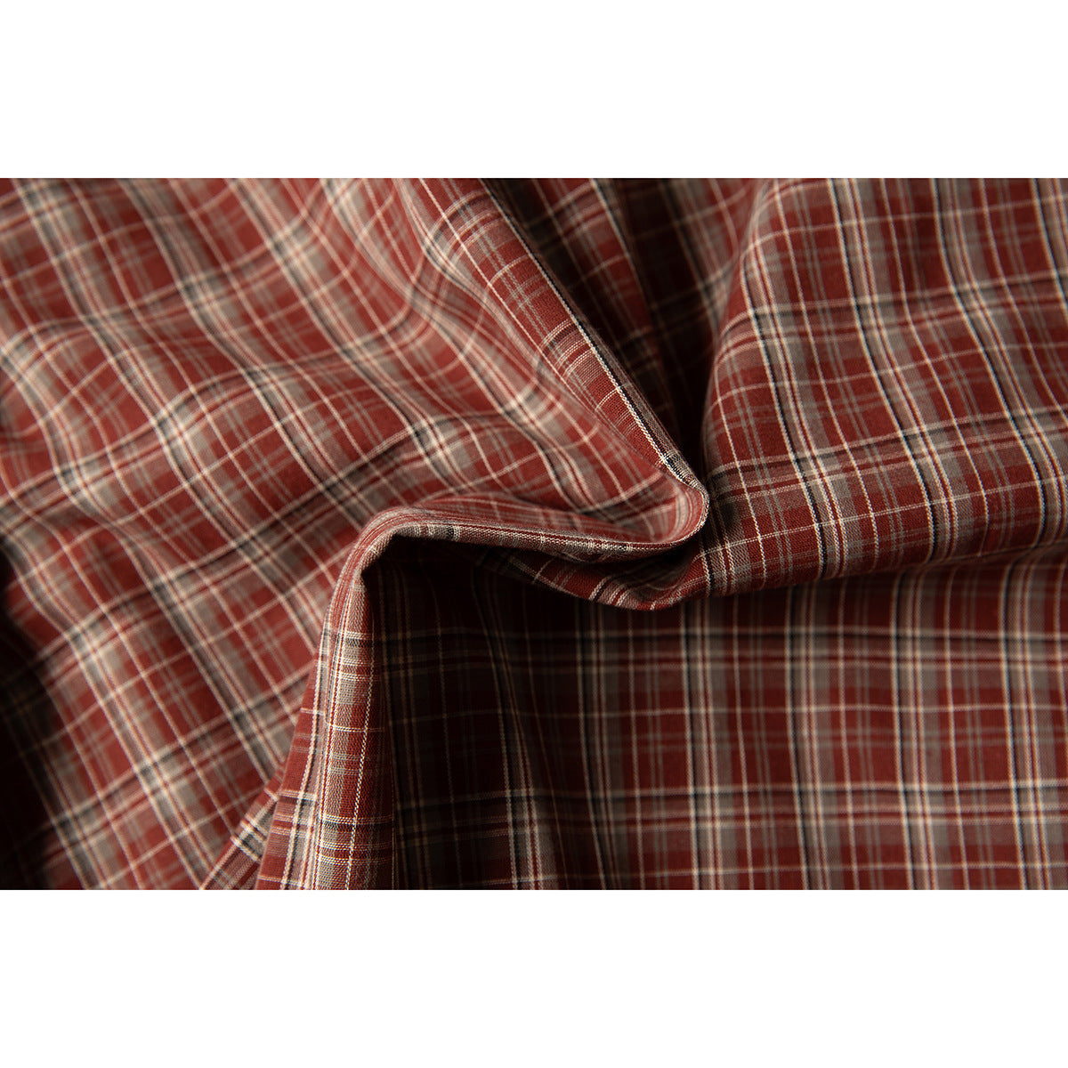 Close-up of rust-red, brown, and cream plaid fabric draped to show its pattern and texture.
