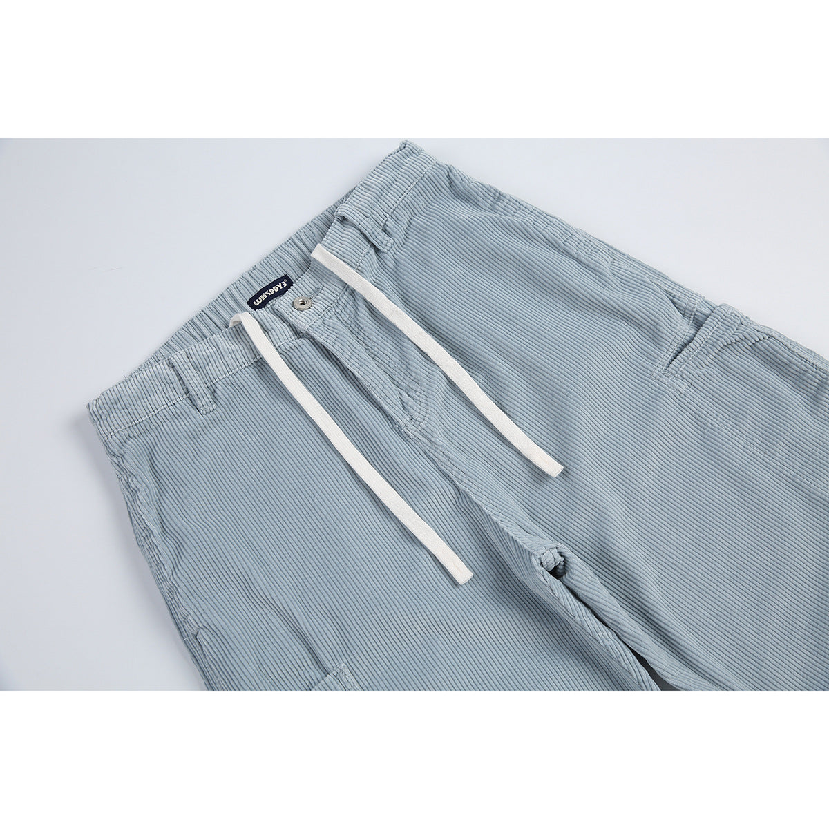 Close-up of light blue ribbed trousers showing the elastic waistband, button, white drawstrings, and front seam.