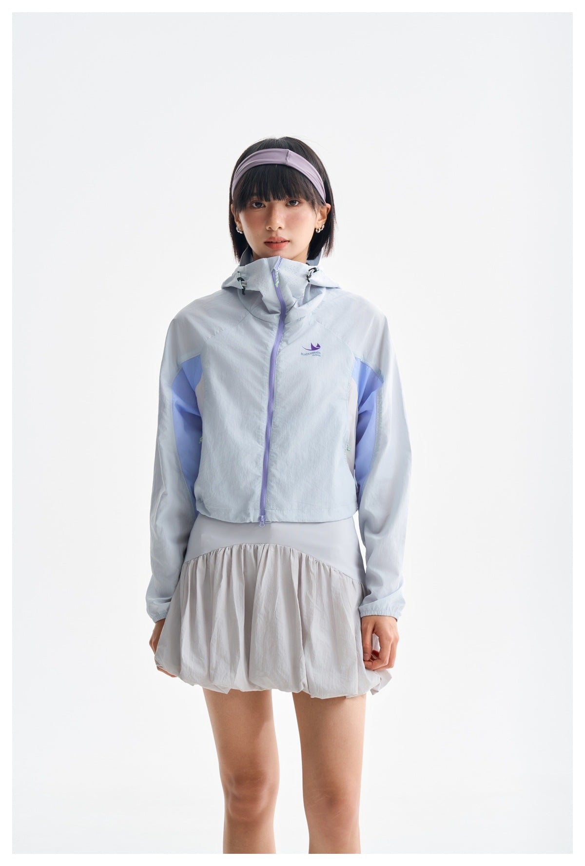 Front view of a model wearing a zipped pale blue hooded jacket with lavender zipper and sleeve panels.